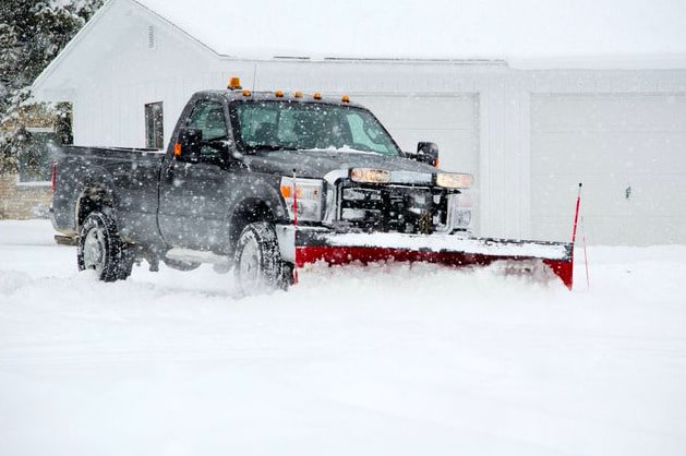 Truck with snow plow clearing a residential driveway during a snowstorm